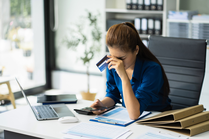 Serious woman cover her face after stressed with credit card debt sit at workplace desk in office use calculator calculates monthly expenses.